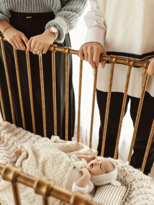 Newborn photography Monsey NY – Parents leaning over a brass crib with their newborn